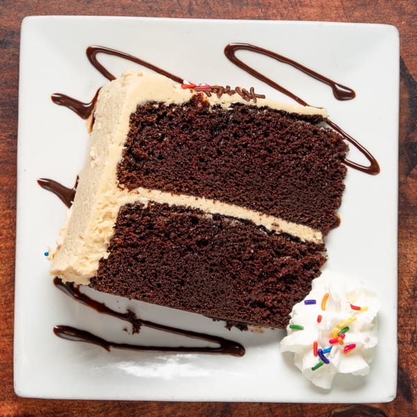Slice of chocolate cake with peanut butter frosting, chocolate drizzle, and whipped cream with sprinkles.