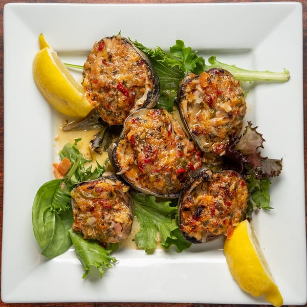 Baked clams with stuffing, garnished with lemon wedges and fresh greens on a white plate.