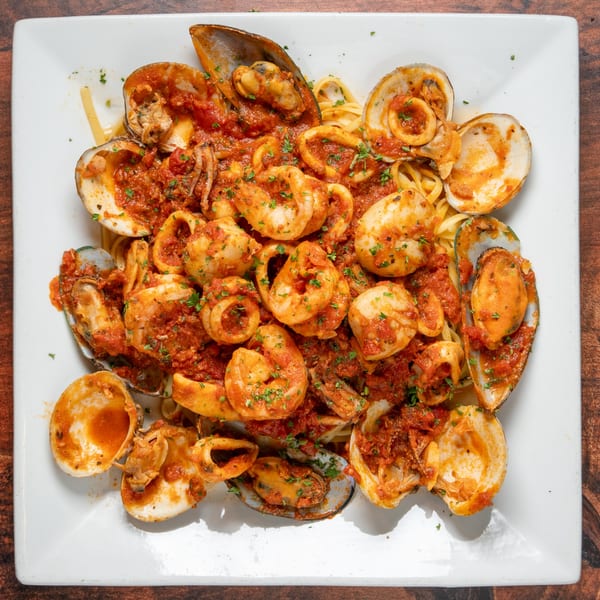 Linguine pasta with shrimp, calamari, mussels, and clams in a rich red sauce, garnished with parsley.