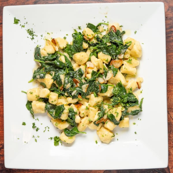 Gnocchi with sautéed spinach, garlic, and parsley on a white rectangular plate.