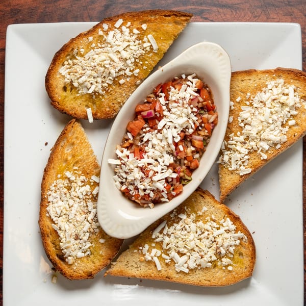 Bruschetta with diced tomatoes, onions, and feta cheese, surrounded by toasted bread on a white plate.